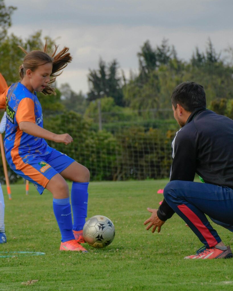 A young girl plays soccer with her coach on an outdoor field, focusing on soccer skills training.