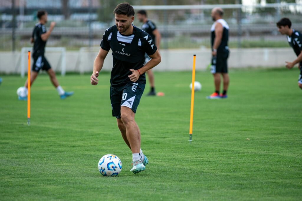 Soccer players training on a grass field, practicing dribbling skills.